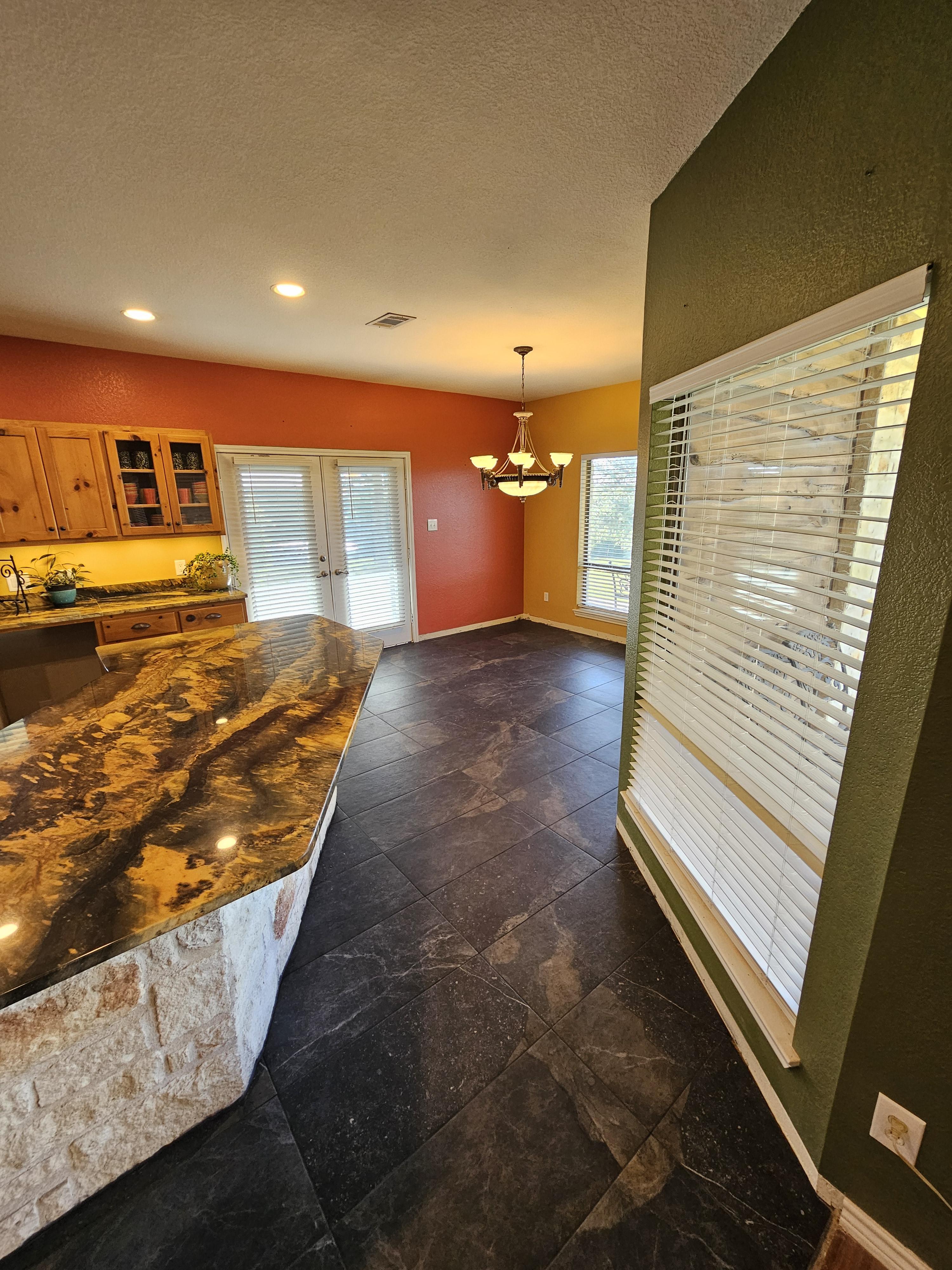 Dark large-format kitchen floor tile extending toward windows and a kitchen island.