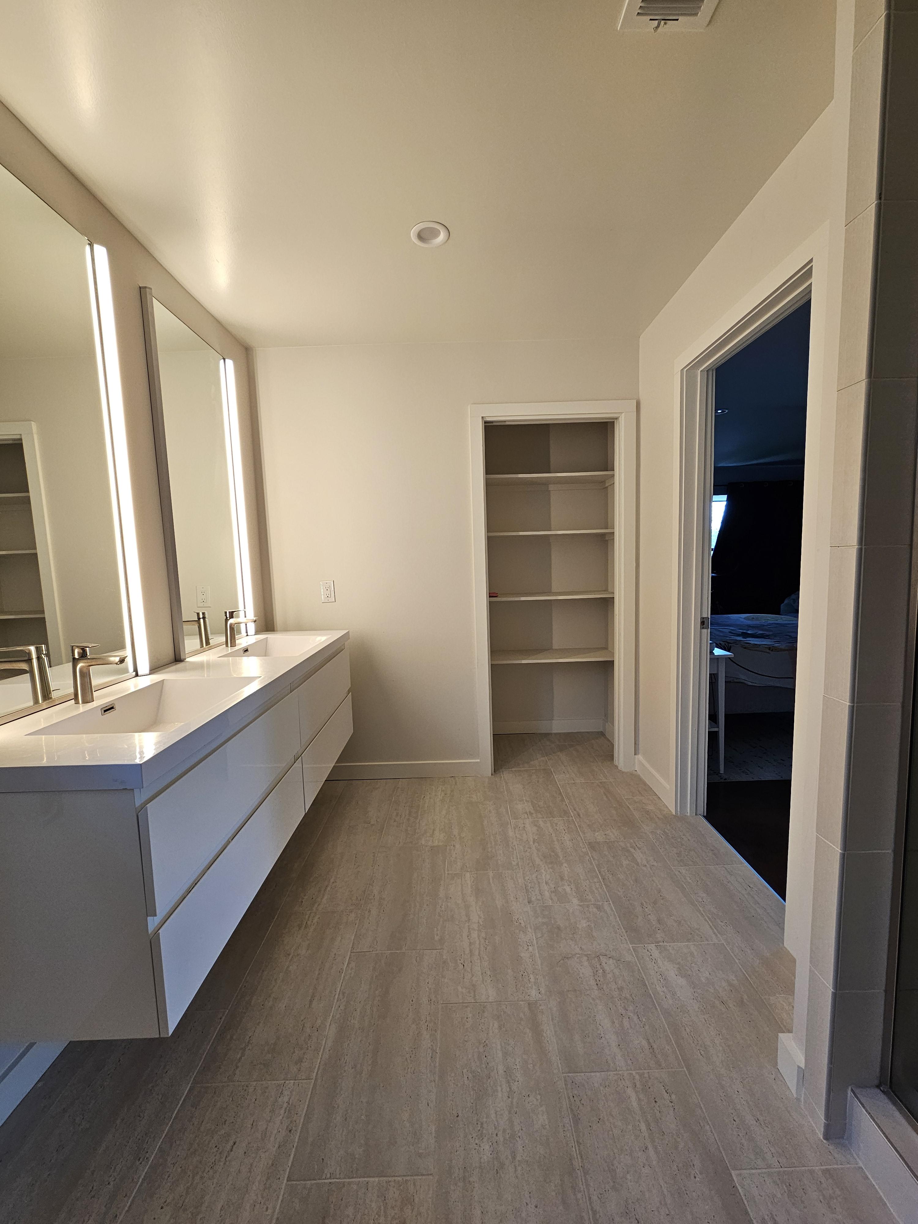 Long view of light bathroom floor tile with a vanity and built-in shelving.