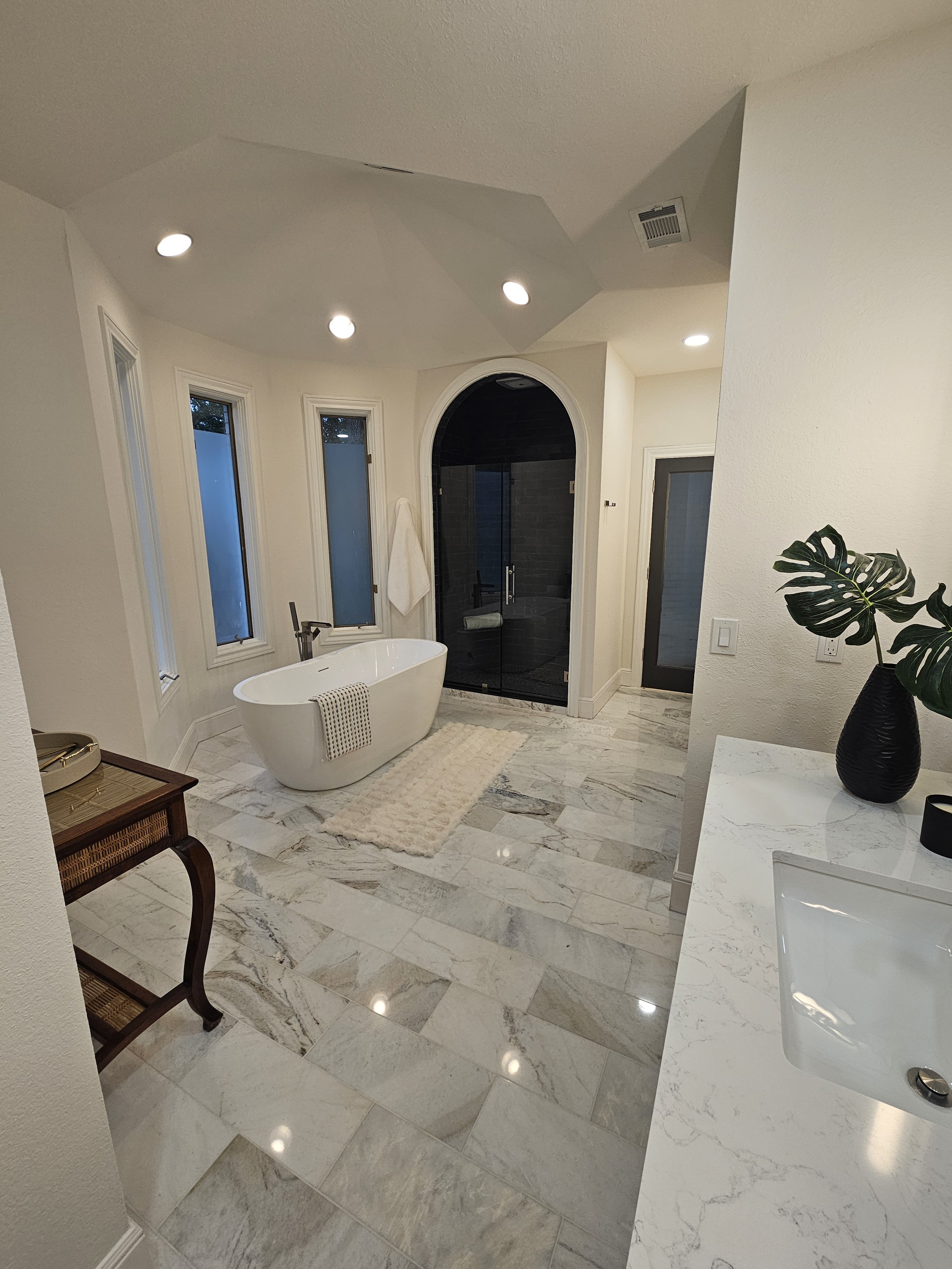 Marble-look bathroom floor tile in a bright bathroom with a freestanding tub and arched shower.